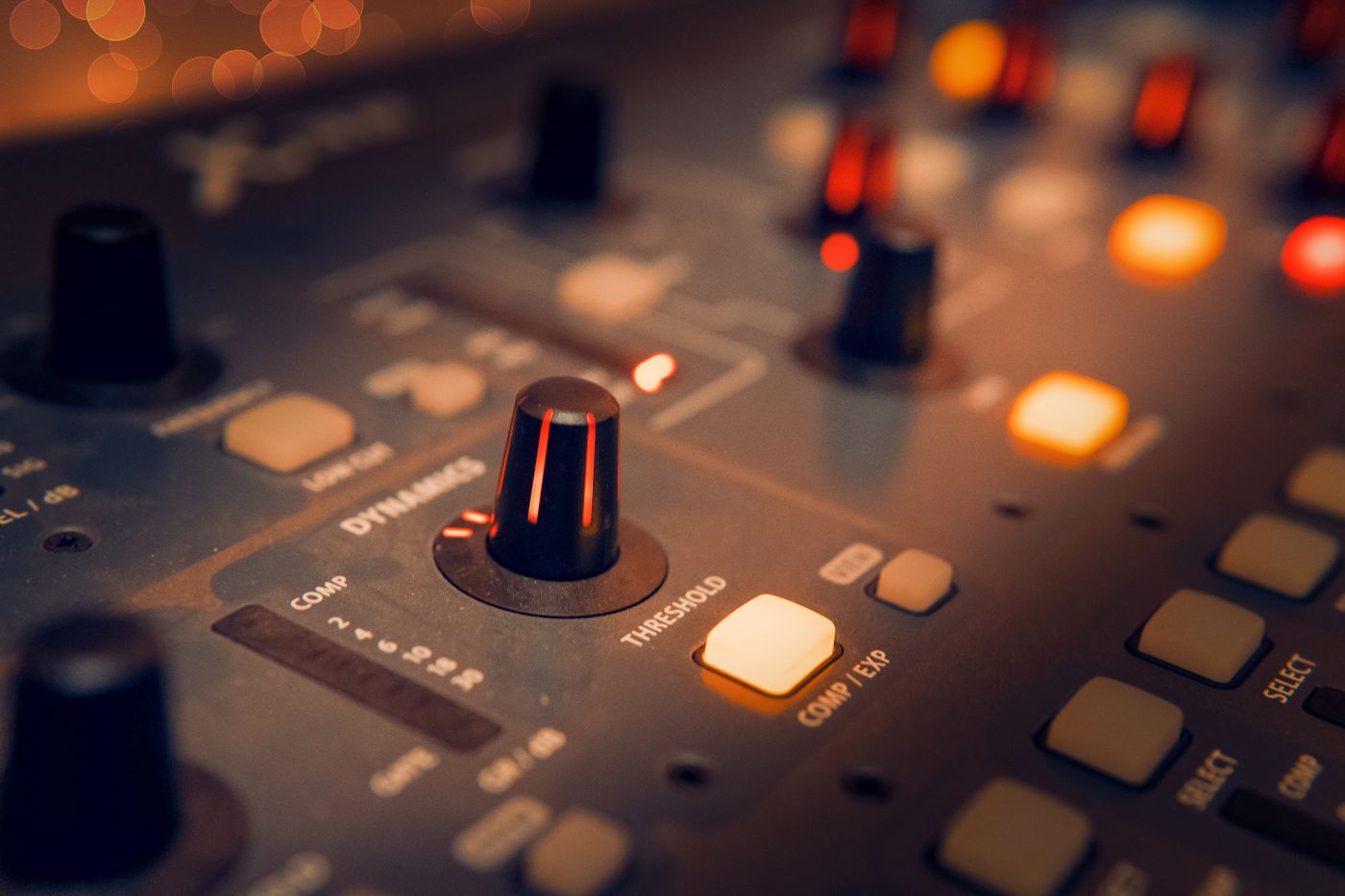 Close-up of a DJ mixer, its knobs and faders glowing in warm amber light